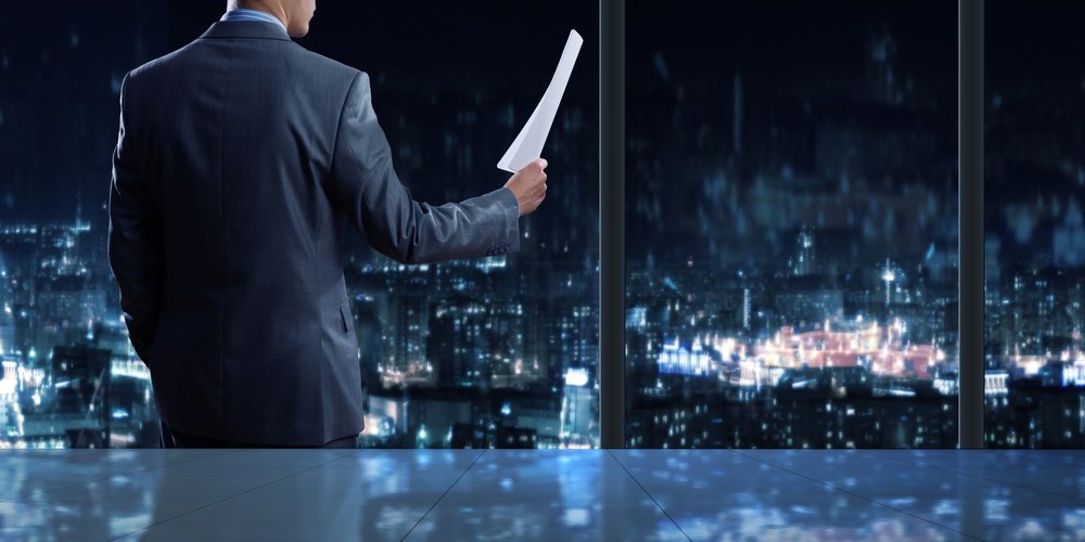 Businessman standing against office window reading documents.jpeg