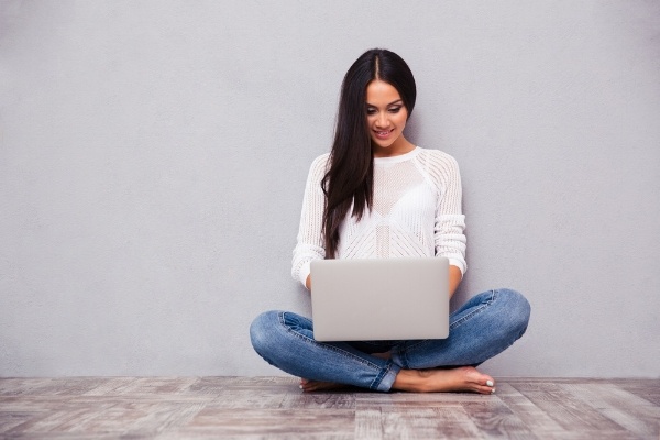 Portrait of a happy casual woman sitting on the floor with laptop on gray background-174870-edited.jpeg
